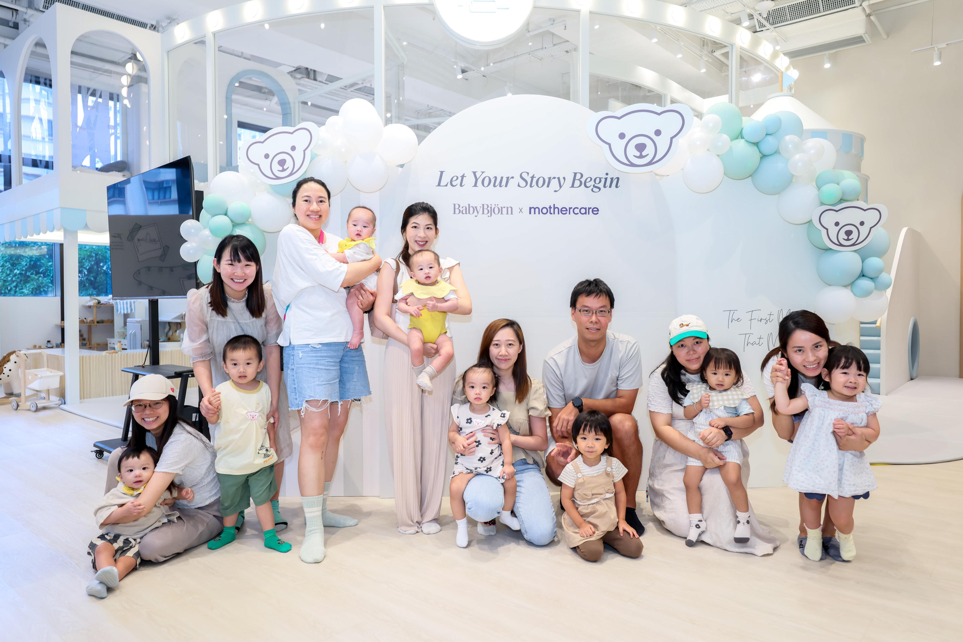 Group of adults and children smiling and posing together in a bright room, with a "Let Your Story Begin" backdrop and balloon decorations.