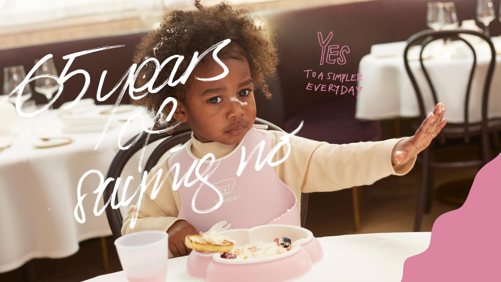 Child with curly hair, wearing a bib, sitting at a table, hand raised, near a plate of food. Text overlays the image.